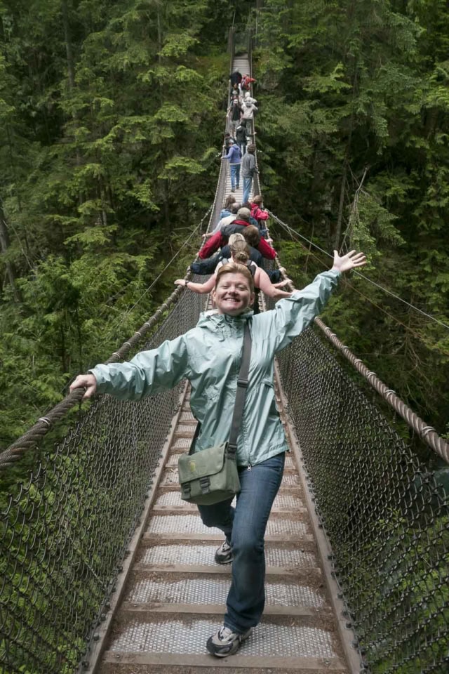 Deb from The Planet D Looking down the long Capilano Suspension Bridge as it stretches across a deep, forest-filled canyon.