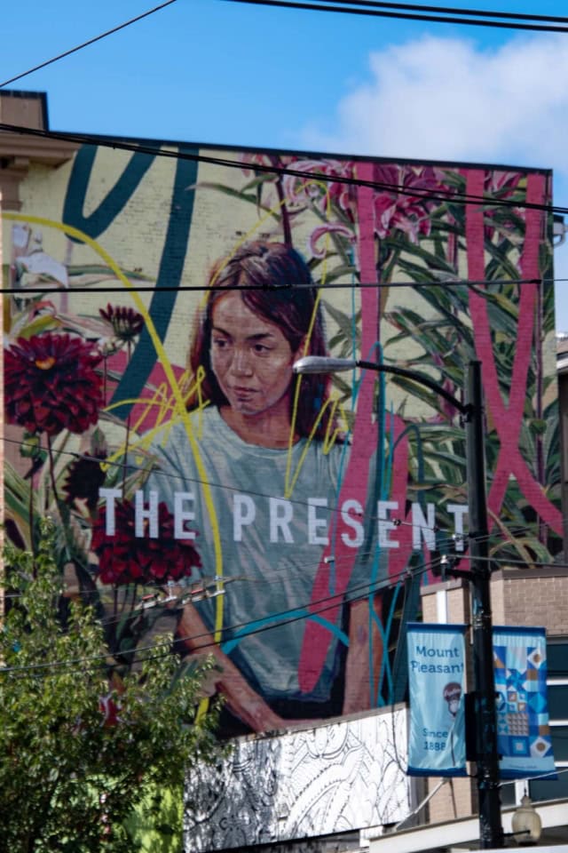 A large, colourful mural of a person's face covering the entire side of a building in Vancouver's Mount Pleasant neighbourhood.