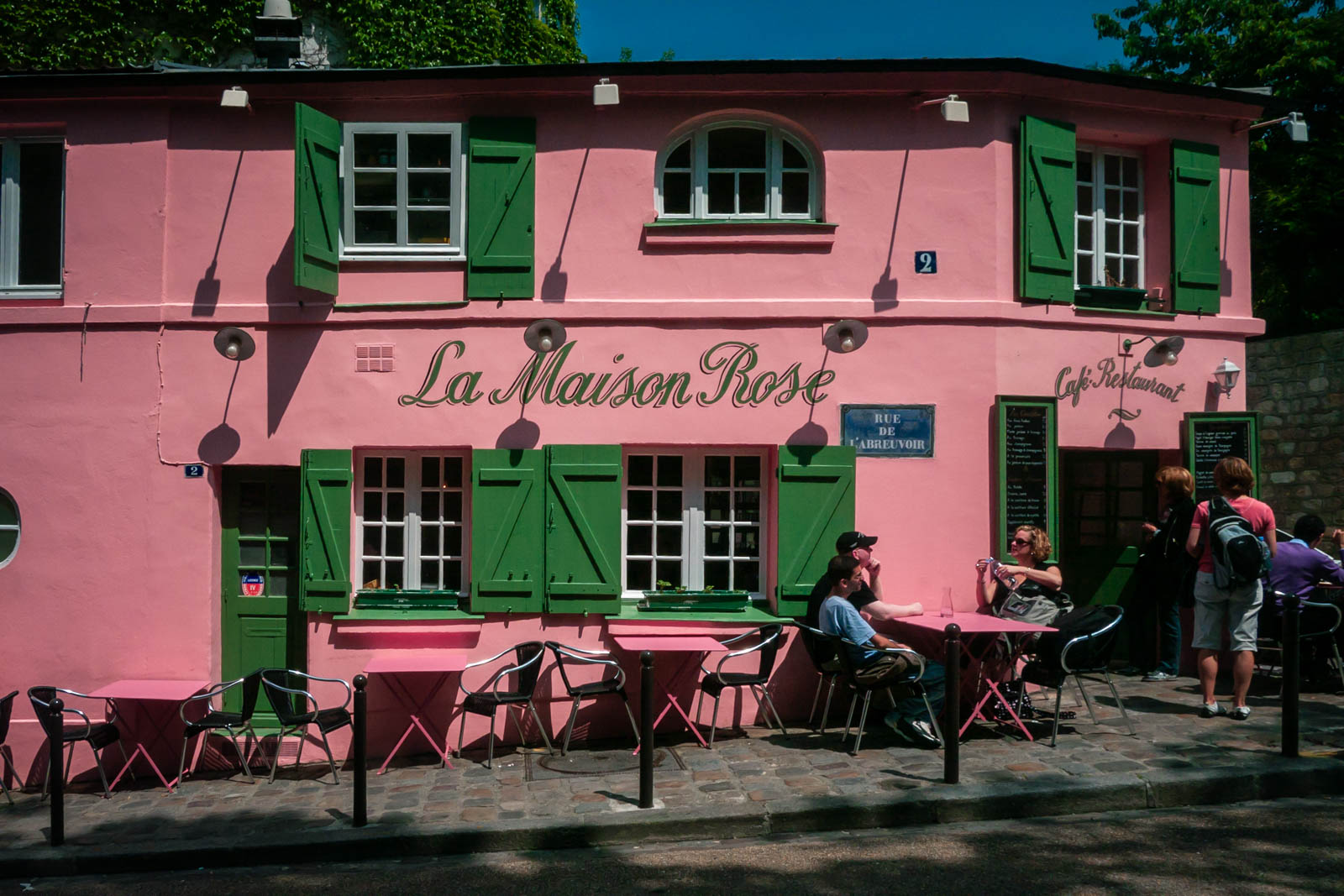 A vibrant, cobblestoned street in the Montmartre neighbourhood of Paris, with people sitting in the cafe.