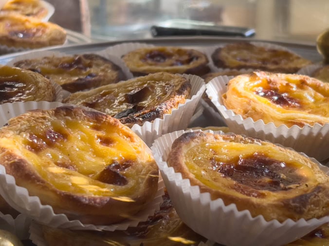 A close-up of a golden-brown Pastel de Nata, a classic Portuguese food, sprinkled with cinnamon.