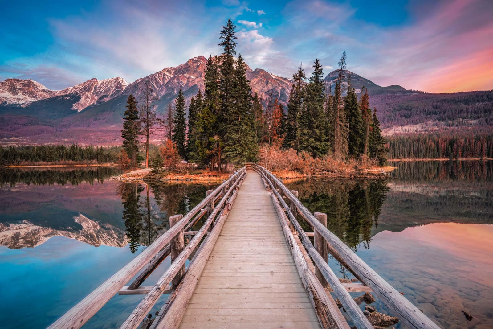 The iconic Pyramid Mountain reflected perfectly in the calm waters of Pyramid Lake, with the wooden bridge to Pyramid Island.